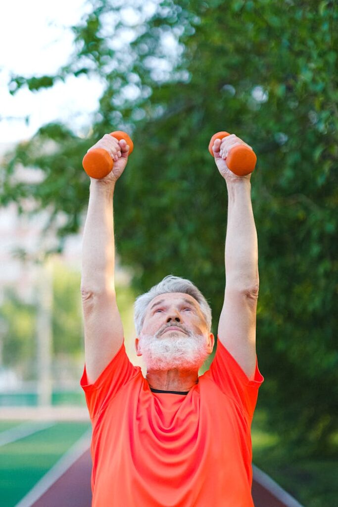 Senior man in sportswear doing exercises with dumbbells on stadium in sunny day